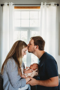 mom and dad hold newborn baby in front of window