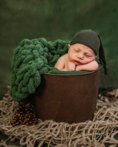 neewborn baby boy in brown bucket with green hat