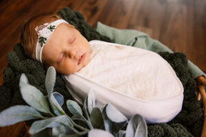 newborn baby swaddled in white and in a basket of greenery