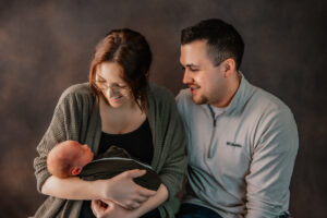 mom and dad look at newborn baby in studio