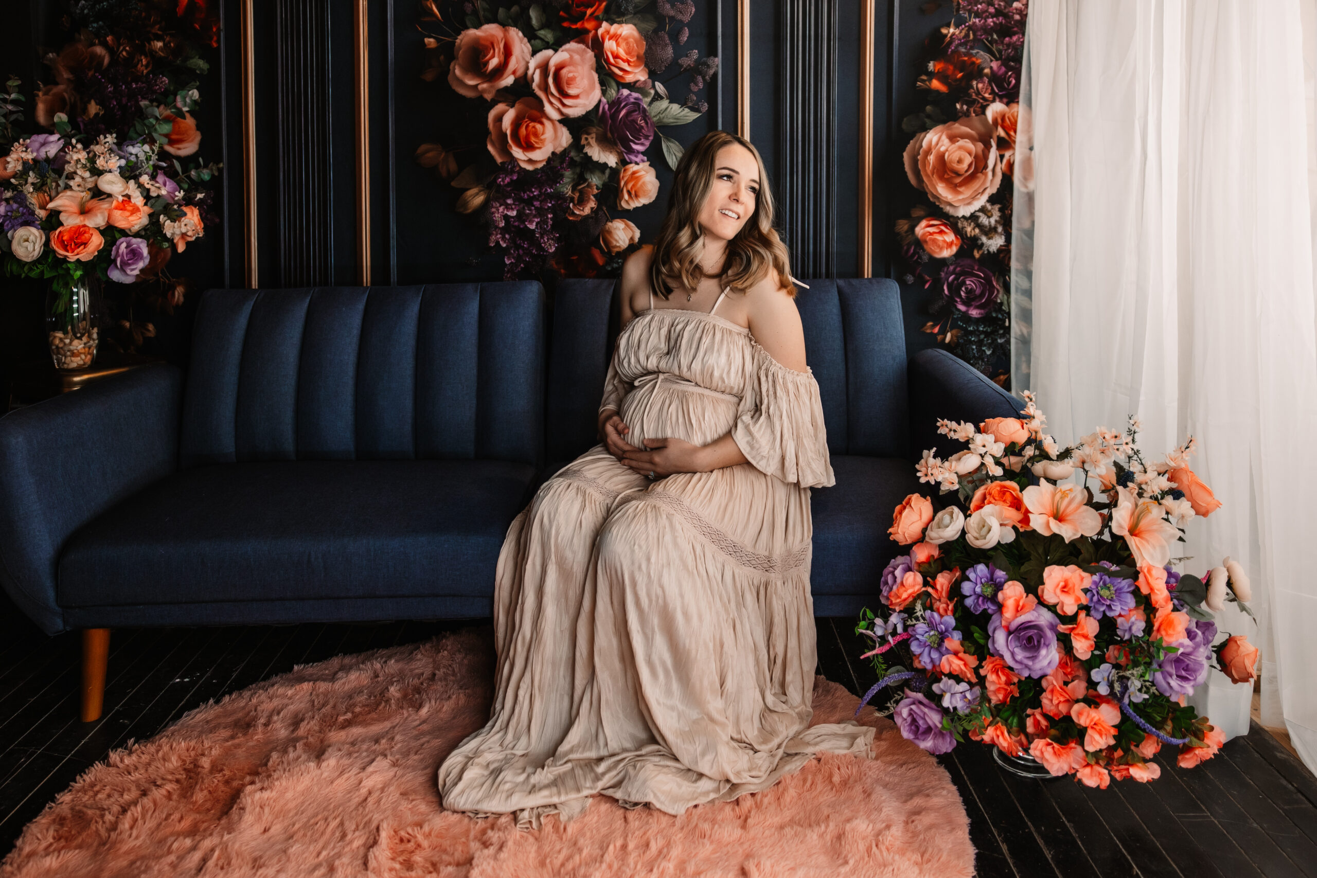 pregnant mom sits in front of floral wall looking to the right