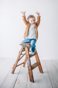 toddler boy shows how big he is on top of ladder