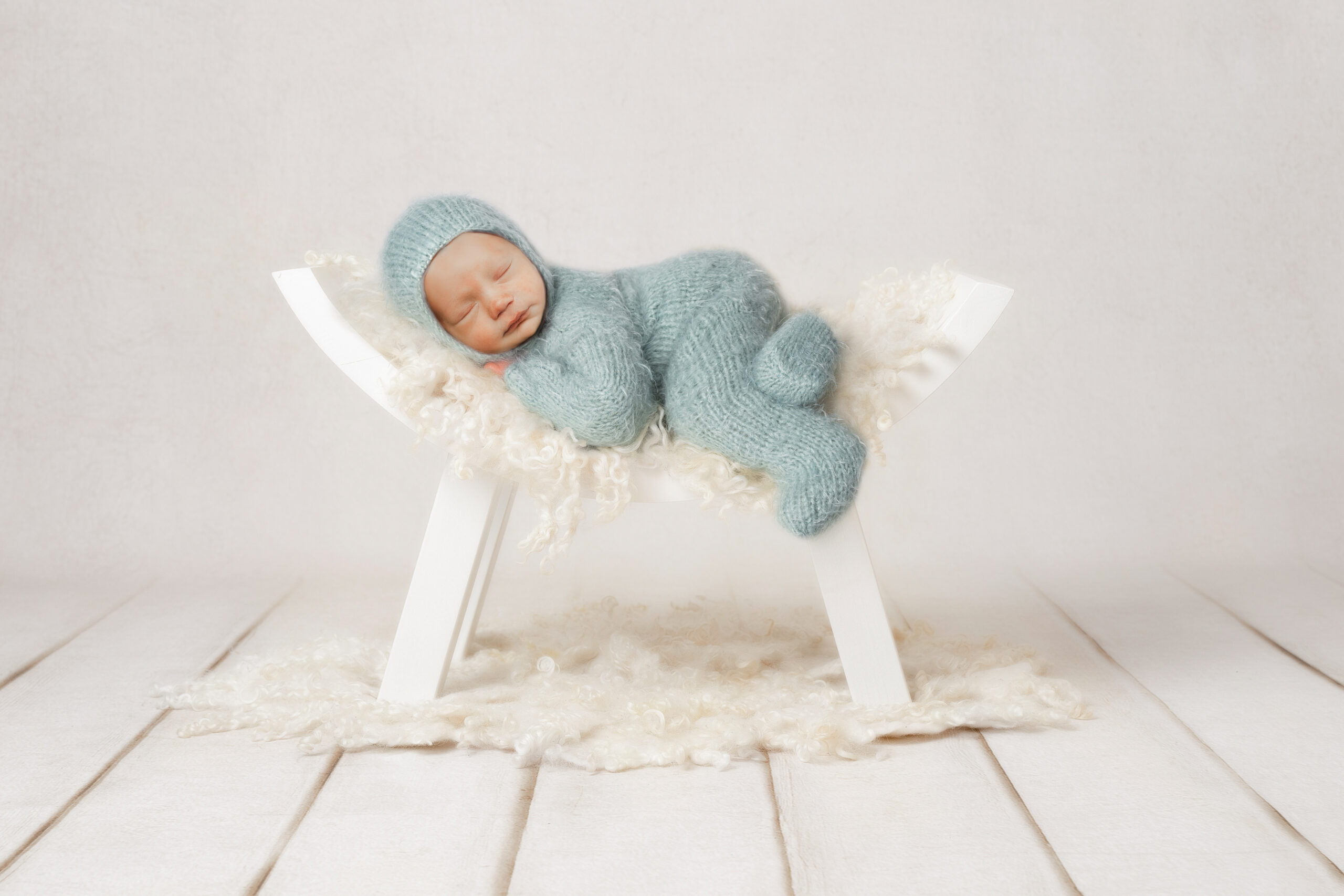 newborn baby in blue sleeping on white bench