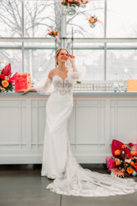 bride stands by bar with pink and orange accents and heart shaped sunglasses